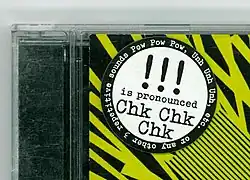 Fokus auf CD-Hülle links oben auf Aufkleber, das !!! als Chk Chk Chk ausgesprochen wird