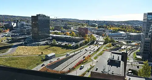 Foto einer Stadt mit einer mehrspurigen Straße in der Bildmitte. Die Straße ist umgeben von mehreren Hochhäusern.