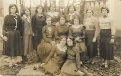 eine Gruppe von 12 jungen Frauen oder Mädchen, einige stehend, andere sitzend (im Hintergrund 1 Mann)