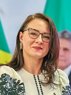 Der Mann wird sitzend und mit Blick an der Kamera vorbei fotografiert. Im Hintergrund ist eine blau-gelbe Fahne zu erkennen.