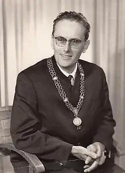 Lächelnder sitzender Mann von vorn und leicht nach links schauend im zeittypischen dunklem Anzug und weißem Hemd mit dunkler Krawatte und einem umgehängten Orden vor der Brust in schwarzweiß.