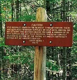 Holzschild mit dem Text „Caution. It is 100 miles south to the nearest town at Monson. There are no places to obtain supplies or help until Monson. Do not attempt this section unless you have a minimum of 10 days supplies and are fully equipped. This is the longest wilderness section of the entire AT and its difficulty should not be underestimated. Good hiking! MATC“
