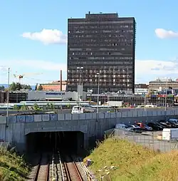 Foto von Gleisen, die in einem Tunnel verschwinden. Darüber ein mehrstöckiges Hochhaus.