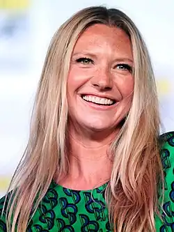 Anna Torv lächelt auf der San Diego Comic-Con 2012. Sie trägt ein grünes Kleid mit einem auffälligen Muster aus blauen und schwarzen Formen. Ihr blondes, langes Haar ist offen. Der Hintergrund ist unscharf, möglicherweise mit Bannern oder Schildern, die zur Comic-Con gehören.