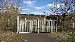 Eingangstor, daneben ungezügelte Vegetation von etwa 25 Jahren