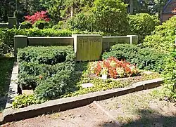 Das sehr große Grab ist mit grünen Pflanzen bewachsen. Der Stein ist hell und Quadratisch. Die Inschrift lässt sich nicht erkennen, da der Stein aus der Ferne fotografiert wurde, um die Dimension des gesamten Grabes zu erfassen.