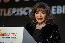 Joan Collins an einem Rednerpult