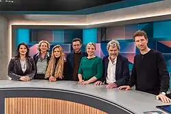 Gruppenfoto mit sieben Personen vor Studiokulisse