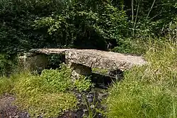 Eine Brücke aus zwei dicken Steinplatten überspannt einen Bach