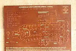 Eine rostbraune Metalltafel. Der Grundriss der Kathedrale ist als Relief erhaben und somit auch tastbar dargestellt, die Beschriftung ist in Normalschrift (weiß auf rostbraunem Grund) und in Brailleschrift ausgeführt.