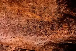 Tänzer-Fries in Agrour Amogjar. Dunkle Strichmännchen auf braunem Felshintergrund.
