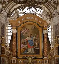 barockes Kircheninterieur, Altar mit gold-roten Säulen, in der Mitte ein monumentales Heiligengemälde, auf dem Ludwig, rot-blau gewandet, und von Engeln umgeben ein Kreuz hält.