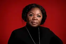 Porträt einer schwarzen Frau vor rotem Hintergrund, die mit ernstem Gesicht in die Kamera blickt