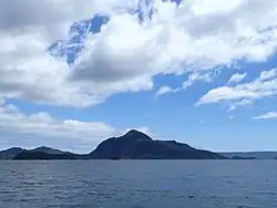 Panoramablick über das Meer auf die Insel mit ruhiger See und blauen aber bewölkten Himmel.