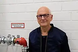 Porträt von Andreas Neumeister vor weißgestrichener Ziegelwand, 2022