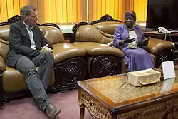 Der ehemalige deutsch Politiker Jan van Aken im Gespräch mit Ann Itto Leonardo. Ein Europäischer Mann in dunklem Anzug und eine afrikanische Frau im violetten Kostüm sitzen nebeneinander in barock anmutenden, pompösen Sesseln.