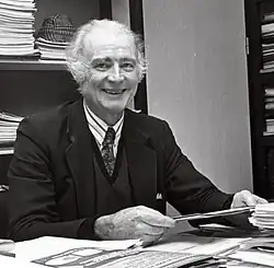 Schwarzweiß-Foto: Duijvestijn sitzt an seinem Schreibtisch und lächelt freundlich in die Kamera