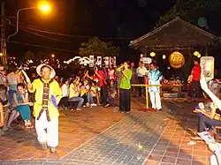 Auf einem Platz ohne Hütten gespielt: zwei Hieu im Hintergrund, ein Helfer trägt eine gelbe Fahne zu einem Spieler