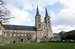 Barocke Kirche mit zwei hohen Türmen und Uhr, umgeben von historischen Gebäuden auf dem Michelsberg in Bamberg.