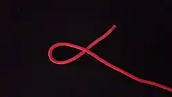 Man legt mit dem rechten (hier rot) Ende von rechts nach links ein Linksgängiges Auge. Das heißt, das lose Ende (hier rot) wird entgegen dem Uhrzeigersinn unter das Seil gelegt.