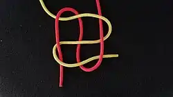 Dann fährt man in der Draufsicht von rechts oben kommend mit dem anderen Ende (hier rot) unter, über und nochmal über das hier zur Vereinfachung gezeigte gelbe Ende, wendet und unter, nochmal unter und nochmal unter wieder zurück, wendet wieder und über, nochmal über und unter wieder nach unten.