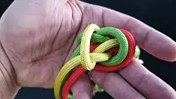 Nun muss der Knoten noch in der richtigen Reihenfolge angepasst werden. Am besten bringt man die einzelnen Kardeele so in Form, dass der Überhandknoten in die Mitte zeigt. Hier das gelbe Kardeel