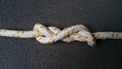 Man zieht leicht an beiden Enden des Seiles oder Fadens, der Knoten dreht sich beim Zuziehen um sich selbst