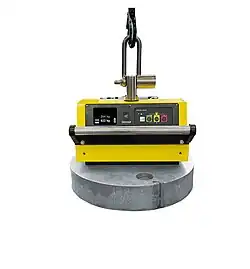 Das Bild zeigt einen modernen batteriebetriebenen Lasthebemagneten mit Display, Modell SB950-SF. Er hebt und transportiert große, runde Metallteile. Der Magnet misst die Magnetkraft, vergleicht sie mit dem Werkstückgewicht und zeigt auf dem Display an, ob das Werkstück transportiert werden kann.