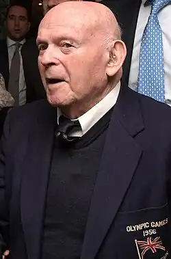 Ben Helfgott im dunkelblauen Blazer mit der Aufschrift Olympic Games 1956 und der britischen Fahne darunter im Alter von über 90 Jahren. Er ist kahlköpfig und benutzt ein Hörgerät. Das Foto entstand anlässlich eines Besuchs des israelischen Staatspräsidenten beim FC Chelsea.