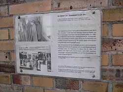 Farbfotografie von einer Gedenktafel mit dem Titel „Depot für Aktion Entartete Kunst“. Rechts steht ein Text und links sind zwei Schwarzweißfotografien. Auf einem betrachtet Hitler die aufgereihten Gemälde im Lager und auf dem zweiten Foto sind die Gemälde ausgestellt.