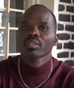 Mann mittleren Alters mit Schnurrbart, der einen roten Pullover und eine Halskette trägt