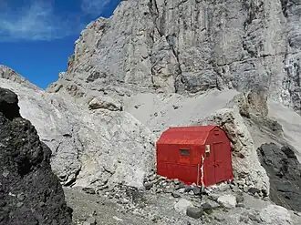 Die Biwakhütte Marco Dal Bianco (2015) im Hintergrund der Passo Ombretta, die Südwand der Marmolata und am linken Bildrand die Forcella Marmolada (2885&nbsp;m)