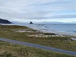Foto eines Strandes, im Hintergrund eine Insel im Meer