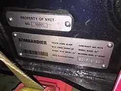 Zwei bedruckte und gestanzte Blechschlder mit Informationen zum Drehgestell. Schild 1: PROPERTY OF NYCT NO. 55021. Schild 2: BOMBARDIER TRUCK TYPE: B-45P CONTRACT NO: R179 / MAX LOAD: 45500 LB WHEEL BASE: 82" / WHEEL SIZE (NEW): 34" BEARING SIZE: 5" BORE / DATE MANUFACTURED: 2016.3.28