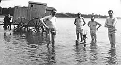 Schwarzweißfoto von 1919: Gruppenbild mit Friedrich Ebert, Gustav Noske und zwei weiteren Männern in Badehosen, im Wasser der Ostsee stehend. Die Männer stehen in einer Reihe und blicken in die Kamera. Ein weiterer Mann liegt unten verdeckt im Wasser.