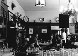 Das Bild zeigt einen Tisch in einem altmodisch eingerichteten Haus, an dem vier Leute sitzen.