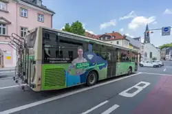 Das Foto zeigt einen Omnibus schief von hinten. Der Bus wartet an einer roten Ampel.