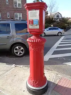 Ein roter Metallkasten, der neben einer Straße auf einem roten, metallenen Podest angebracht ist. Ungefähr in Kopfhöhe einer erwachsenen Person ein Bedienfeld mit zwei nebeneinander angeordneten Klappen: Die linke Klappe ist rot mit einem Symbol für die Feuerwehr, die rechte blau mit einem Symbol für die Polizei. Darunter ist eine kurze Anleitung eingraviert: Man bedient die Säule, indem man die entsprechende Klappe anhebt und einen dahinter angebrachten Knopf drückt. Danach hat man Sprechkontakt mittels eines hinter einem Schutzgitter oberhalb der Klappen angebrachten Lautsprechers und Mikrofons.