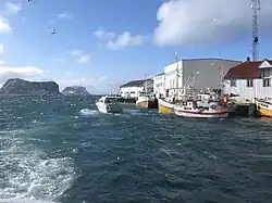 Foto mit einigen Hafengebäuden auf der rechten Seite, einige Boote im Wasser davon und zwei Inseln im Hintergrund