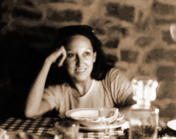 Lonzi an einem Essenstisch mit karierter Tischdecke, nachdenklich lächelnd, Ellbogen aufgestützt