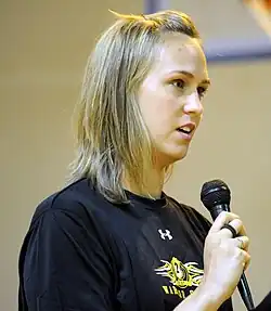 Carly Piper im schwarzen T-Shirt ist im Halbprofil zu sehen. In der rechten Hand hält sie ein Mikrofon zur Beantwortung von Fragen.