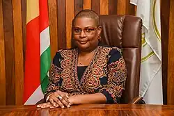 Caroline Abel 2020. Eine untersetzte dunkelhäutige Frau mit kurzgeschorenen Haaren im Saal eines Amtsgebäudes.