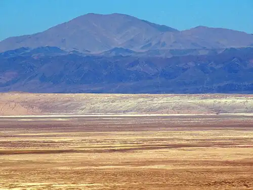 Der Cerro Quimal in ca. 70 km Entfernung vom ALMA OSF (ca. 2915 m ü. M.) aus gesehen. In der unteren Bildhälfte der Salar de Atacama (ca. 2330 m ü. M.) und an dessen Rand die Cordillera de la Sal (< 2600 m ü. M.)