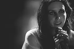 Chelsea Wolfe mit langen schwarzen Haaren in einem weißen Hemd und mit Mikrofon in der Hand, während sie singt