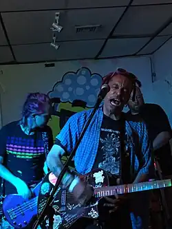 Eng beieinander stehen drei Personen die Instrumente spielen. Mosley steht mit zum Gesang geöffneten Mund hinter einem Mikrofon mit einer mit Stickern beklebten und von Hand beschriebenen E-Gitarre in der Hand. Er hat markante kurze Dreadlocks, die dem zweiten Album seinen Titel gaben, trägt eine Sonnenbrille auf dem Kopf und ein kurzärmeliges kariertes Hemd offen über einem Longsleeve-Shirt. Die anderen Musiker seiner Band sind nicht eindeutig zu identifizieren.