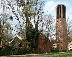 Kirchenbaubörper aus rotem Ziegelmauerwerk, rechts davon der aufsteigende Glockenturm
