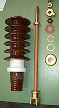 Einzelteile einer DIN-Durchführung (u.&nbsp;a. Porzellan-Isolator und Kupferbolzen mit Anschlussstück)
