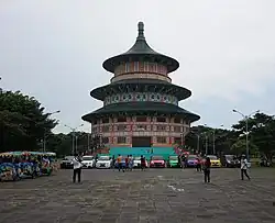 Bild einer chinesischen Pagode, vor der ein großer gepflasterter Platz ist, auf dem Autos und Menschen stehen.