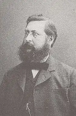 Porträtfoto von Heinrich Züge aus dem Jahr 1885. Zu sehen ist ein Mann mit Vollbart und Brille von der Brust aufwärts, links am Betrachter vorbei blickend.