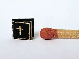 Das Kleinste Buch der Welt in der Variante Vaterunser im Größenvergleich mit einem Streichholz.